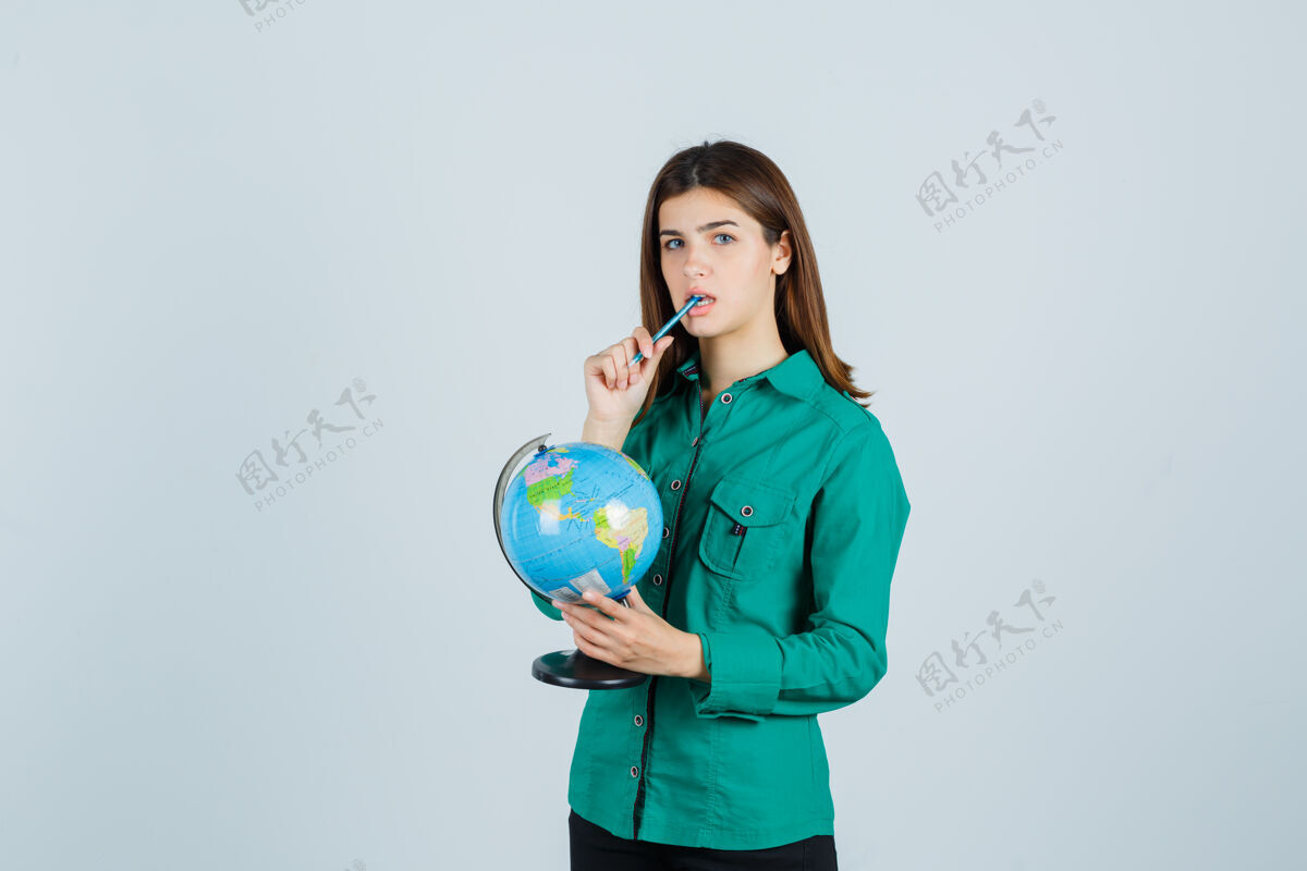感性年轻的女士拿着地球仪 把笔放在衬衫里的嘴里 看着若有所思 俯瞰前方治疗健康举行