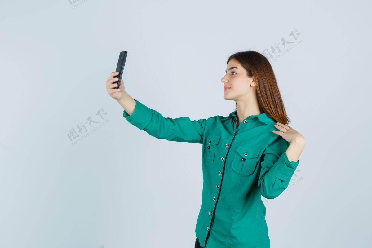 女性穿着绿色上衣 黑色裤子 带着手机自拍的年轻女孩 看起来很开心 正前方的景色自拍采取女孩