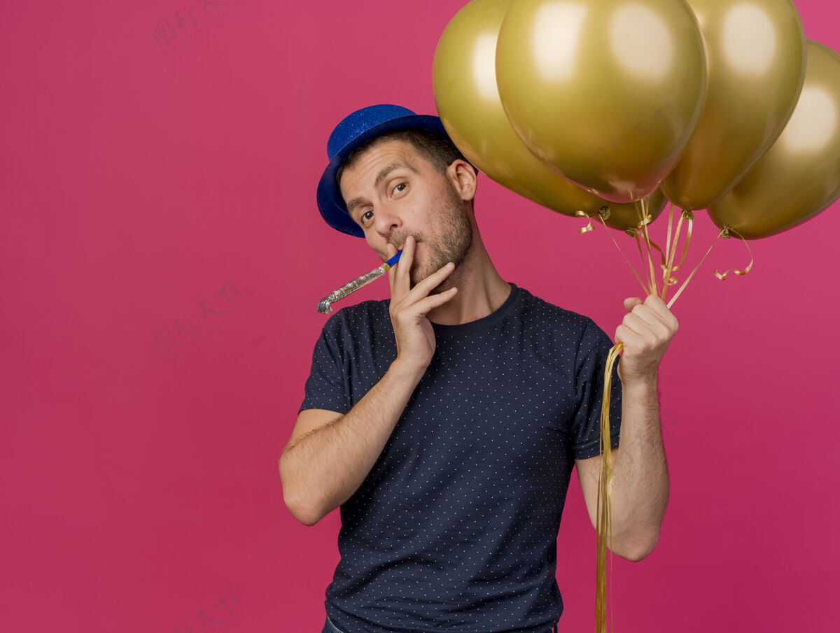 派对戴着蓝色派对帽的白种人帅哥拿着氦气球吹着哨子 粉色背景上留有复制空间粉色吹蓝色
