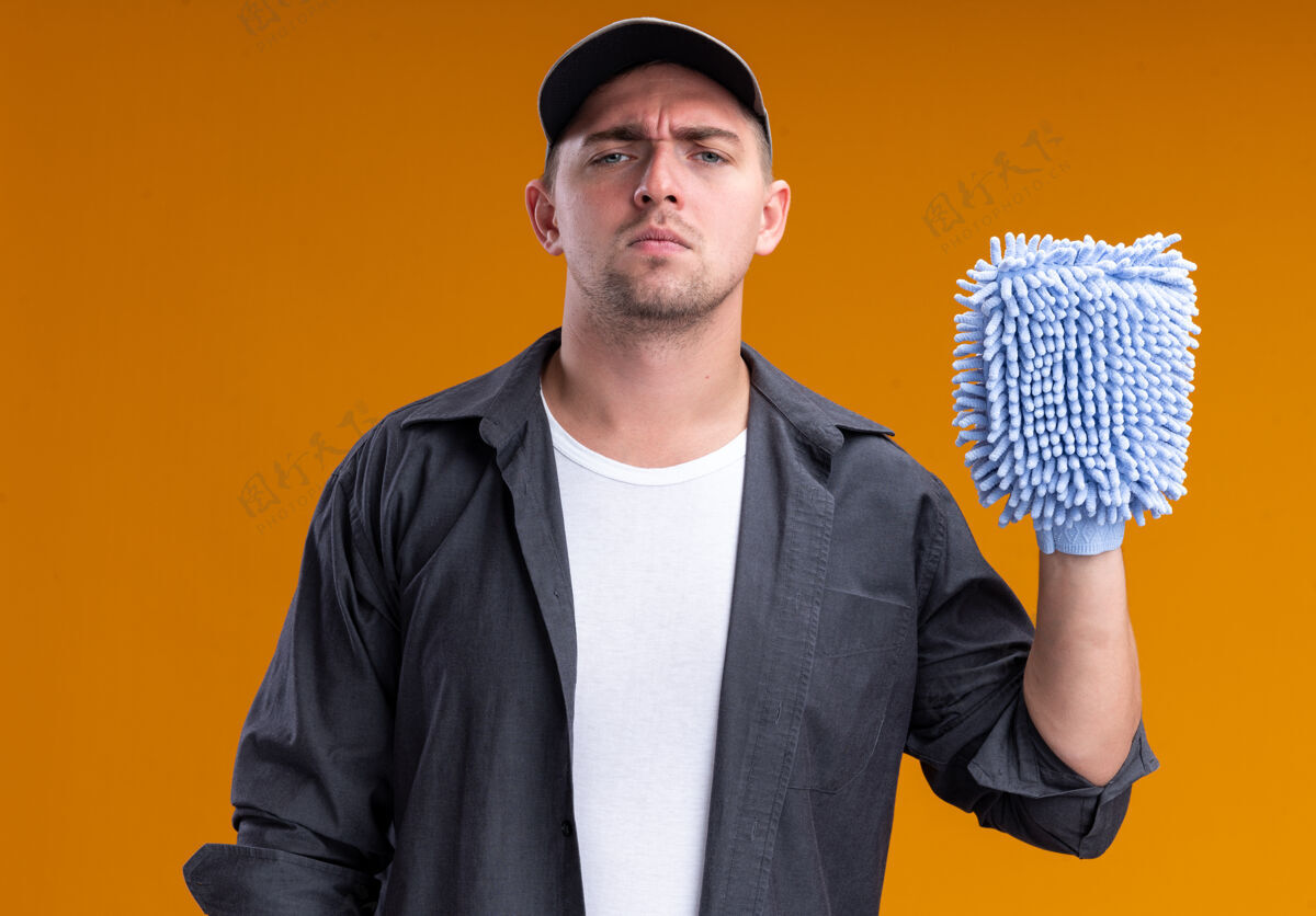 T恤自信的年轻帅气的清洁工穿着t恤和帽子拿着抹布隔离在橙色的墙上自信破布抱着