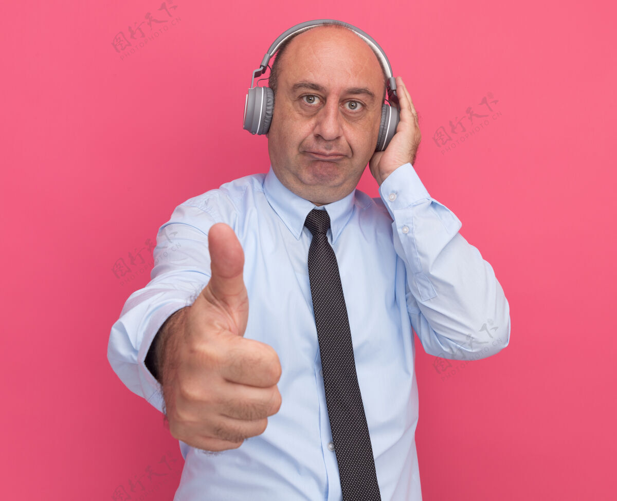 男士一个穿着白色t恤 打着领带 戴着耳机的中年男子在粉红色的墙上孤立地竖起大拇指领带穿中年