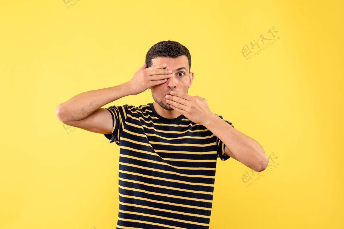 人正面图帅哥穿着黑白条纹t恤 在黄色孤立的背景下遮住嘴巴和眼睛黄肖像条纹