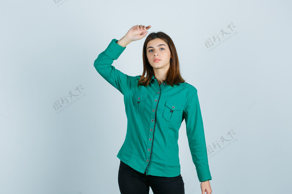 职业年轻女性的肖像摆姿势 同时举起手在绿色衬衫和看起来自信的前视图提高衬衫女士