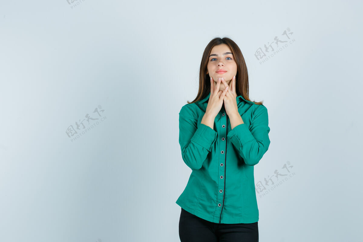 女孩年轻的女性用手指抚摸着下巴 穿着绿色的衬衫 裤子 看起来很可爱 正面图女性女士模特