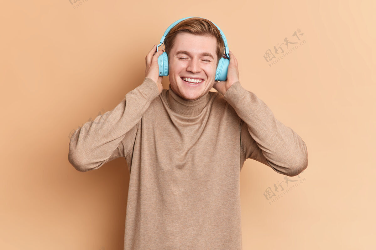 歌曲快乐的男少年轻松地唱着好歌 戴着立体声蓝色耳机 带着灿烂的笑容 想穿着休闲的高领毛衣跳舞娱乐快乐酷