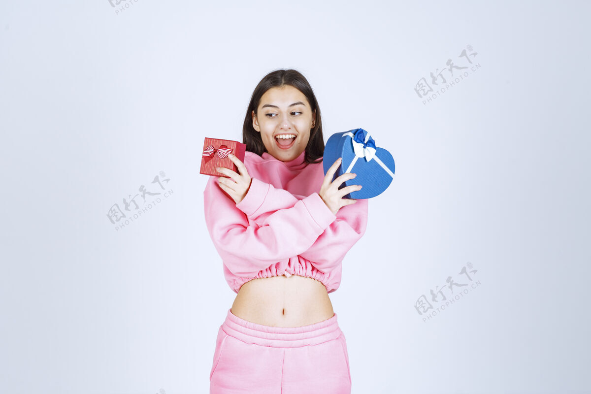 年轻穿着粉色睡衣的女孩双手捧着红蓝相间的心形礼盒成人积极姿势