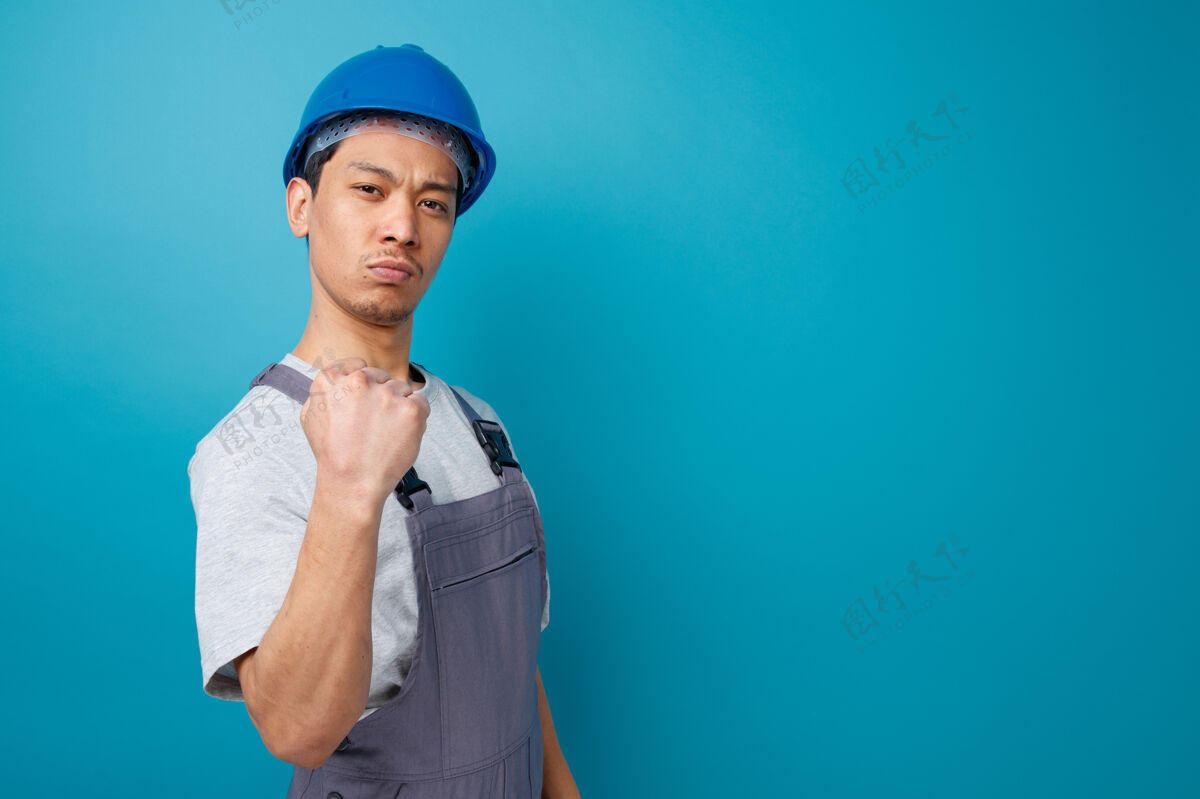 复制自信的年轻建筑工人戴着安全帽和制服站在侧视图做着“是”的手势自信蓝色个人资料