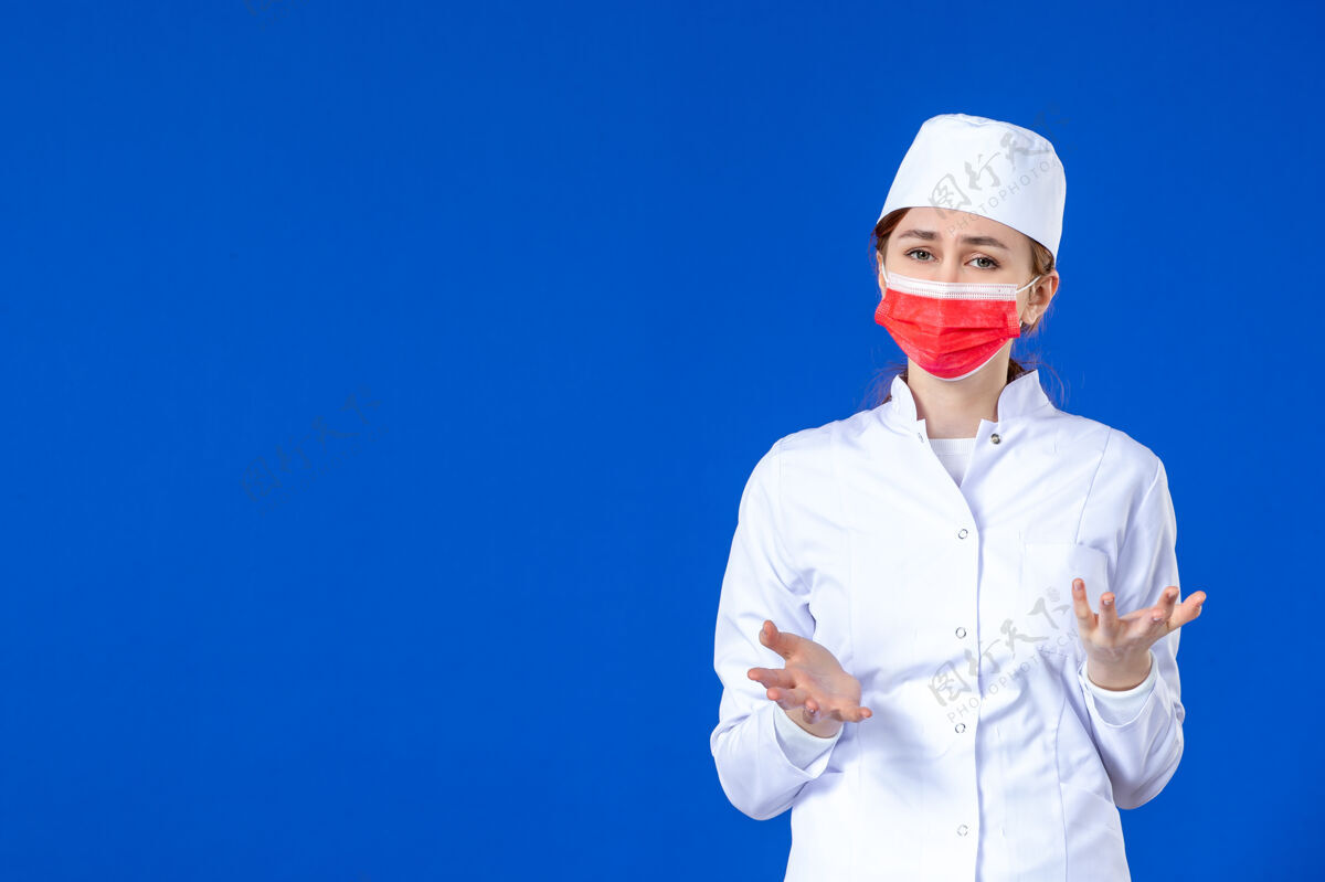 西装压力重重的年轻护士的正视图 身着医疗服 蓝色面罩上戴着红色面罩医药病毒帽子