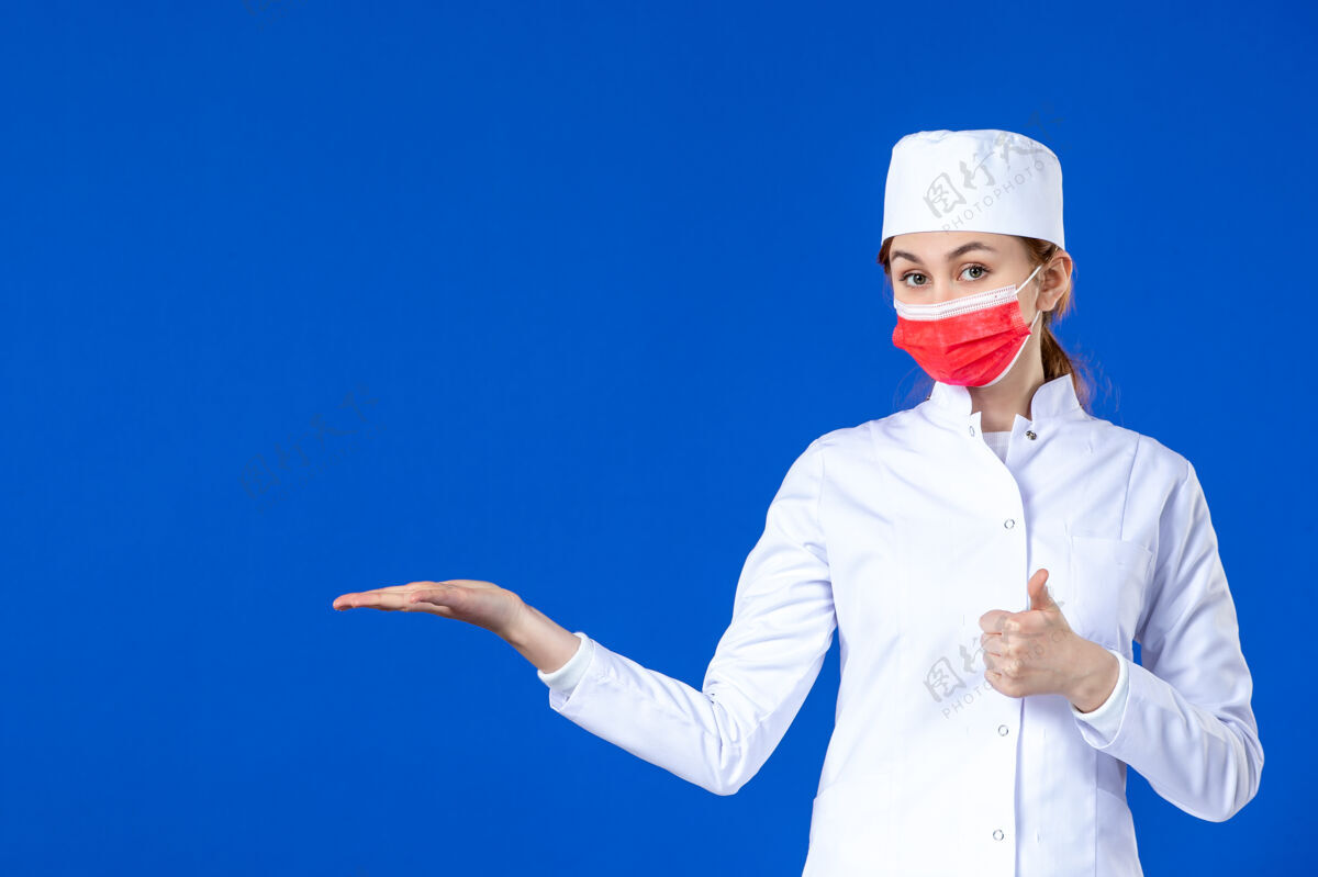服装身穿医疗服的年轻护士的正视图 蓝色的面具上有红色的面具医院流行病职业