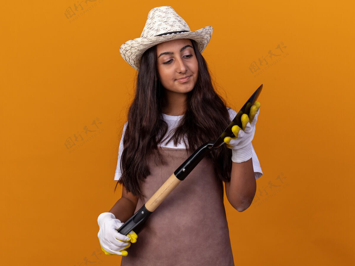 铲子年轻的园丁女孩拿着铲子 自信地看着它站在橙色的墙上花园年轻表情