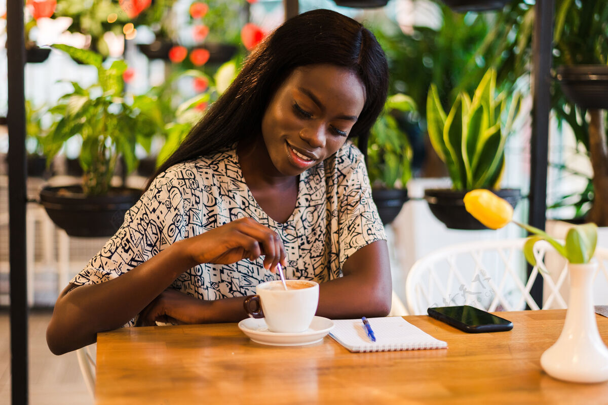 忙碌在咖啡馆喝咖啡的快乐的年轻黑人妇女的特写肖像真实时尚卷发