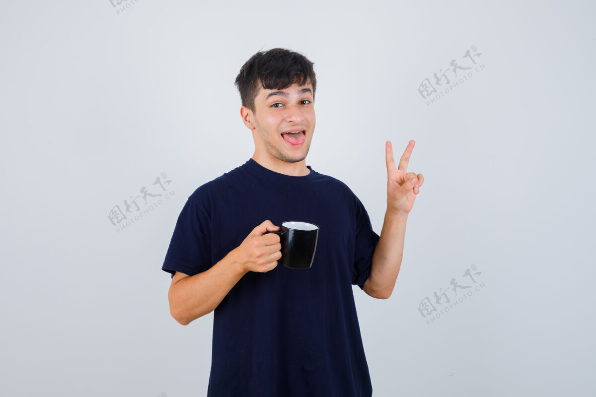 抱着一个穿着黑色t恤的年轻人手里拿着一杯茶 露出v型标志 看上去很高兴 正对着前方自信Vsign人