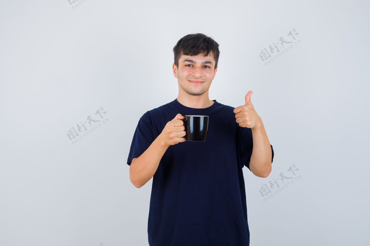 休闲年轻人手里拿着一杯茶 穿着黑色t恤 竖起大拇指 看上去很高兴正面图喜悦衬衫积极