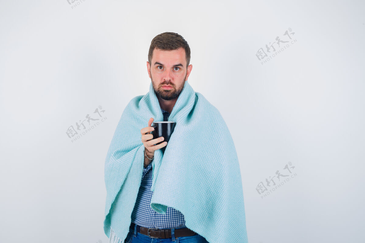 人物年轻的男性拿着杯子 一边看着相机 穿着衬衫 牛仔裤 毛毯 神情严肃正面图人时尚水平