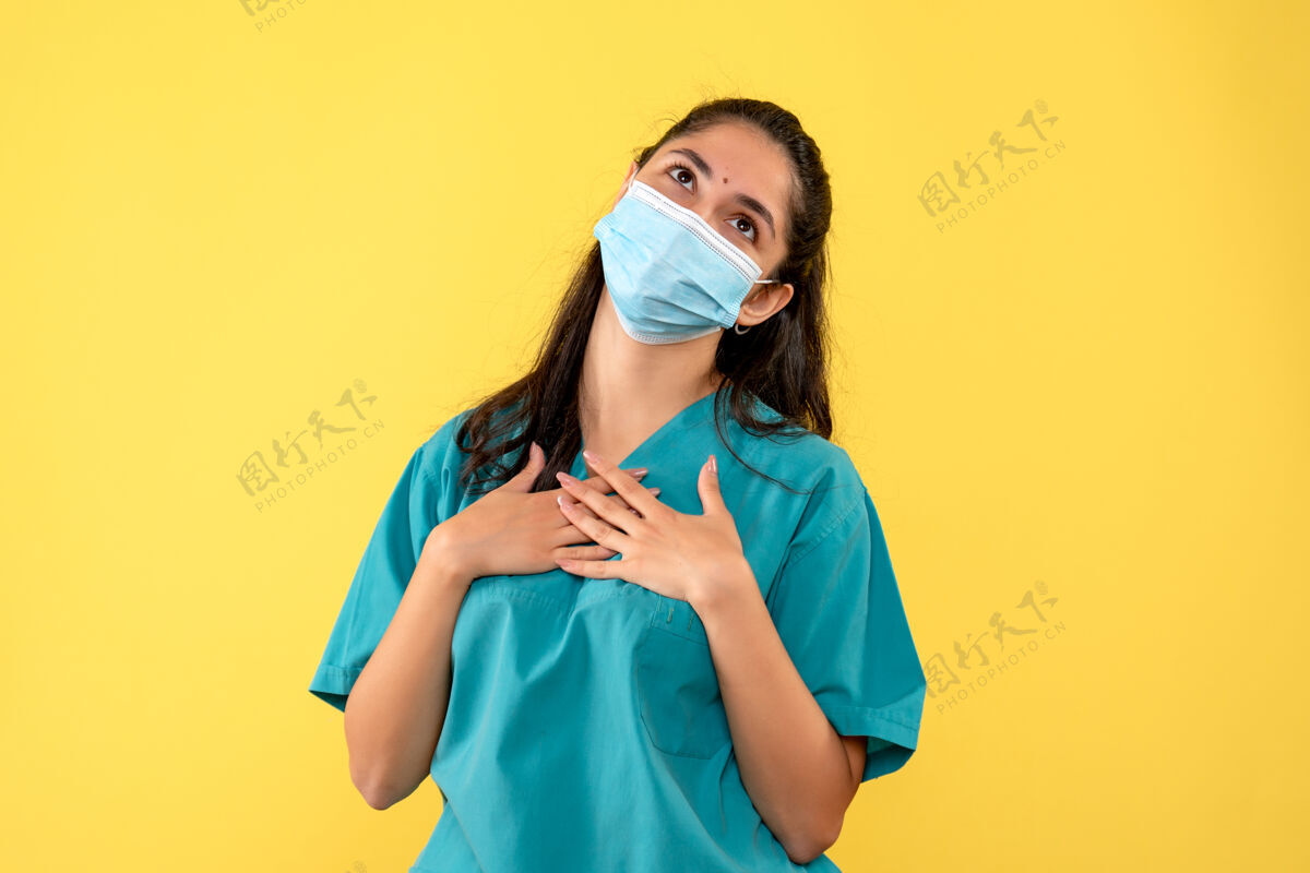 背景前视图：黄色背景下戴着面罩双手放在胸前的女医生微笑正面成人