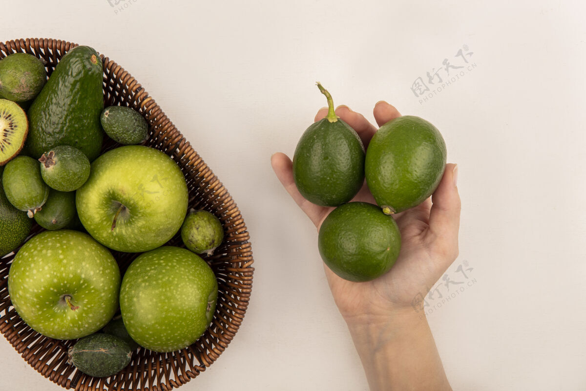 鳄梨女性手拿着新鲜的酸橙和一桶新鲜水果的俯视图 如苹果 鳄梨在白色的表面上美味饮食桶