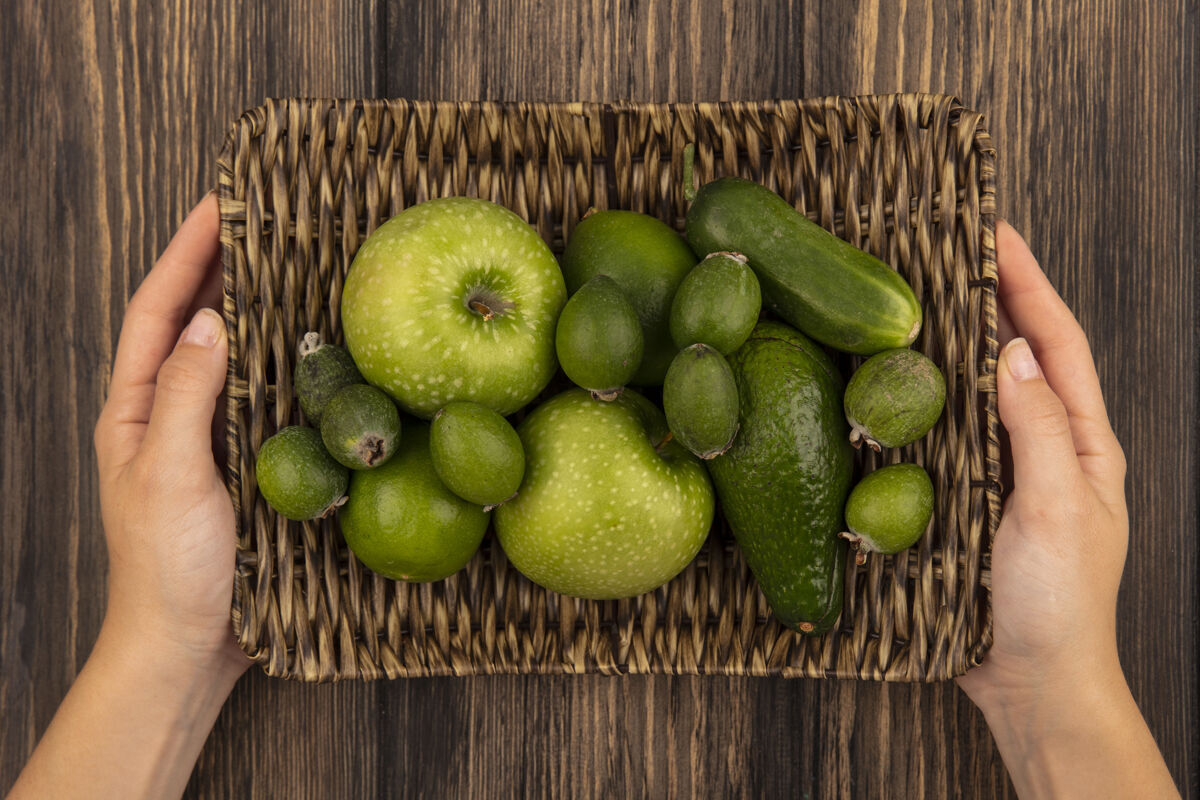 水果顶视图中的女性手拿着柳条托盘的新鲜水果 如绿色的苹果 在木制表面上的酸橙农业手素食