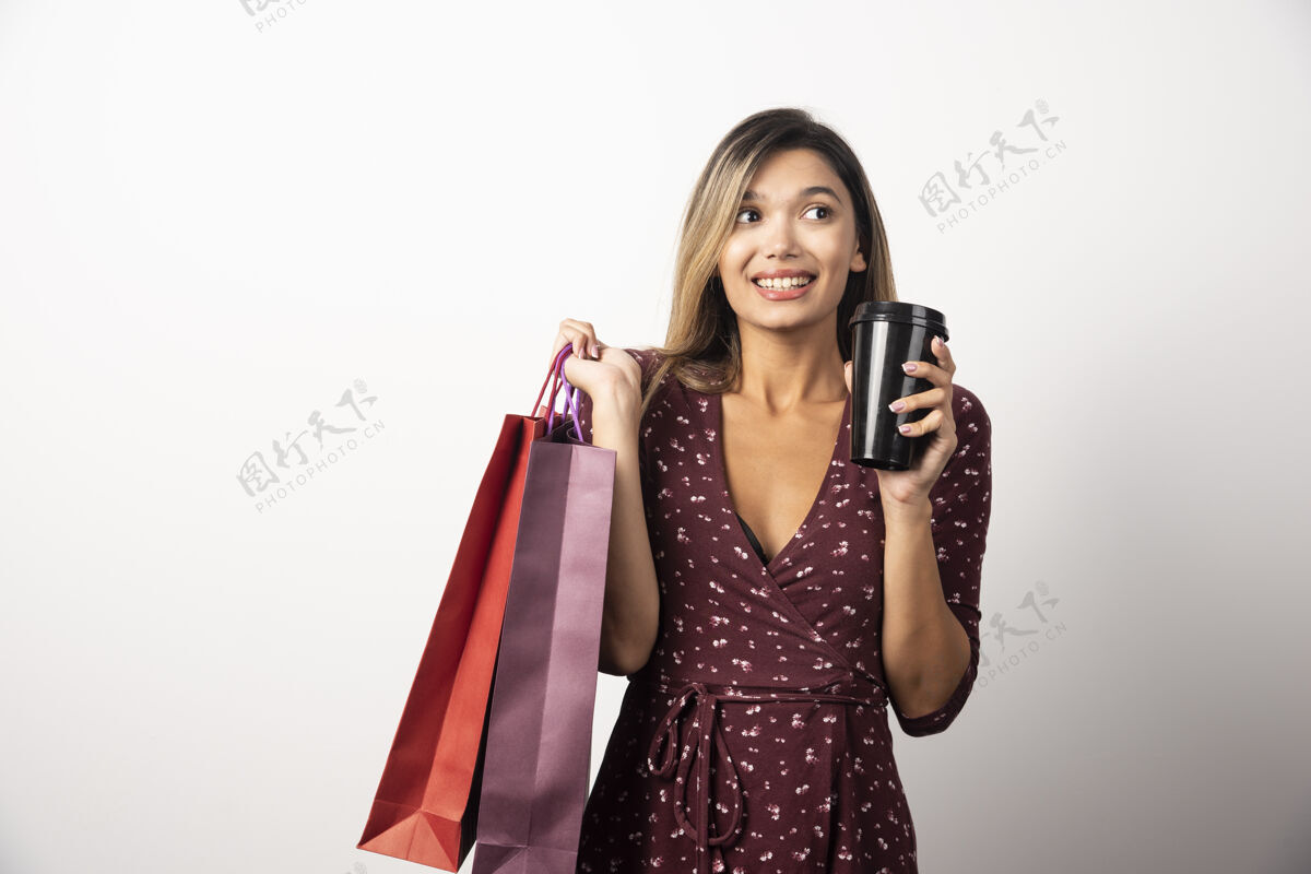茶白墙上拿着购物袋和饮料的年轻女子美味女性模型