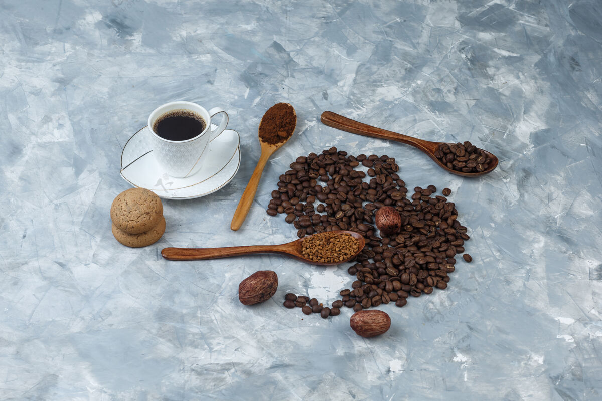 饼干咖啡豆 一杯速溶咖啡 咖啡粉 咖啡豆在木制勺子 曲奇饼高角度查看浅蓝色大理石背景卡布奇诺香味人