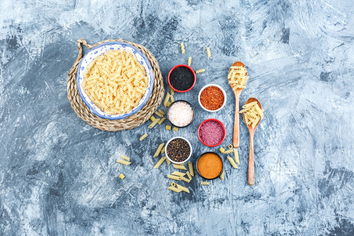 香料一套香料 木勺和意大利面放在一个碗里 背景是灰色石膏和柳条垫顶视图传统晚餐木材