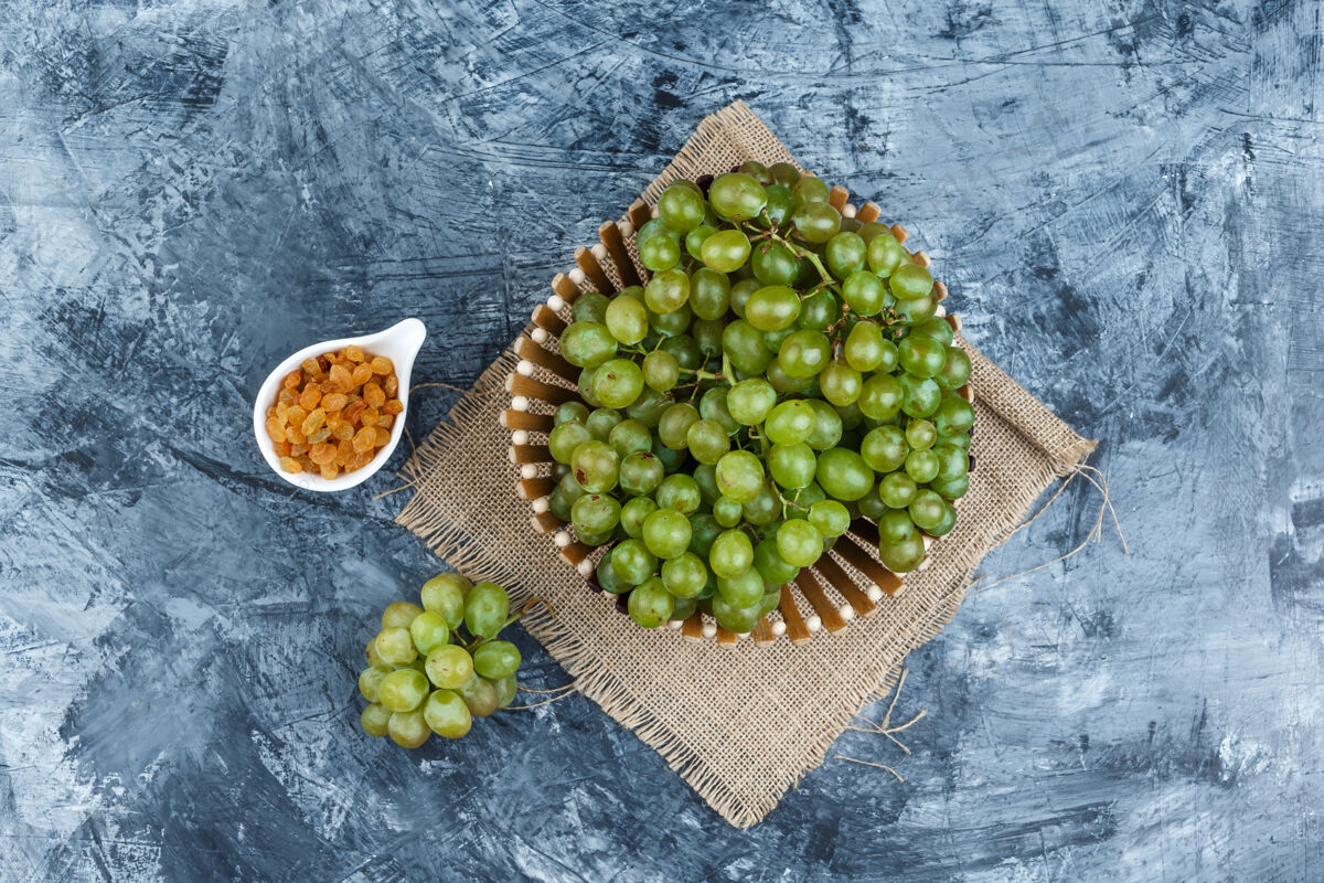 健康一些绿色的葡萄和葡萄干放在一个篮子里的垃圾和一块布袋的背景上 平放着卷须有机路径