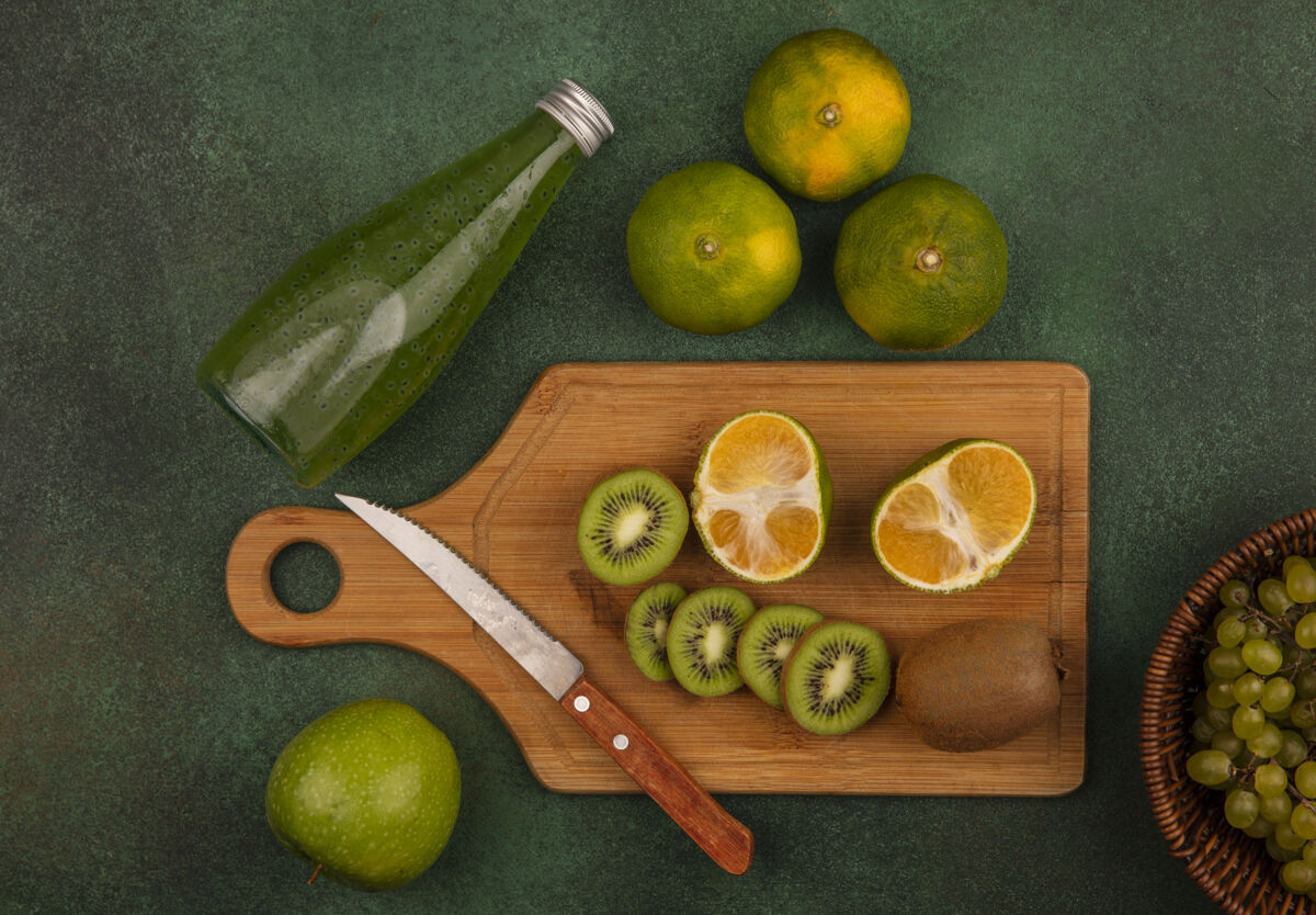 切片顶视图猕猴桃片用刀放在砧板上 橘子和果汁瓶放在绿色的墙上板橘子果汁