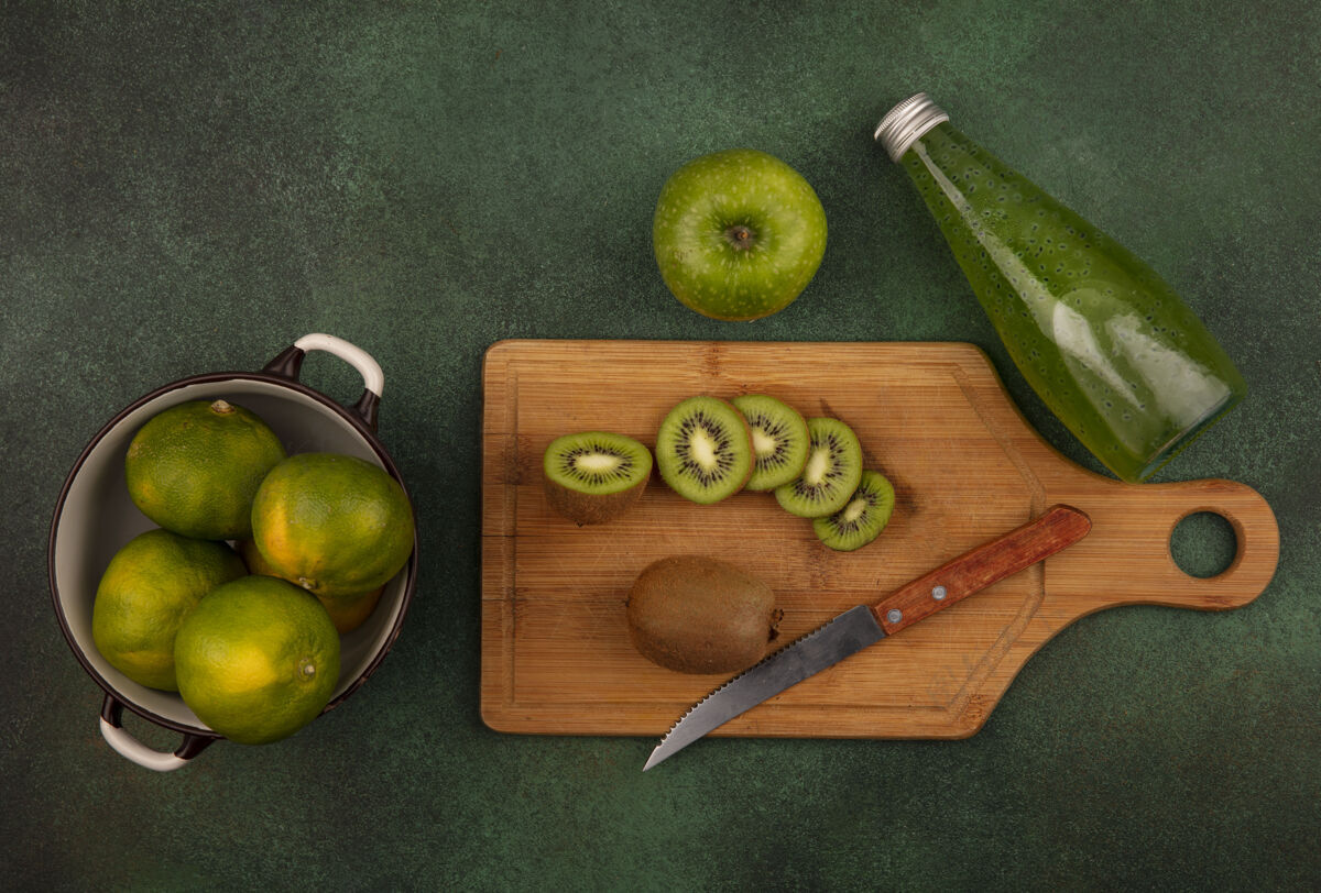 水果顶视图猕猴桃切片用刀在砧板上与橘子在平底锅和一瓶果汁在绿色的墙上切片食物切