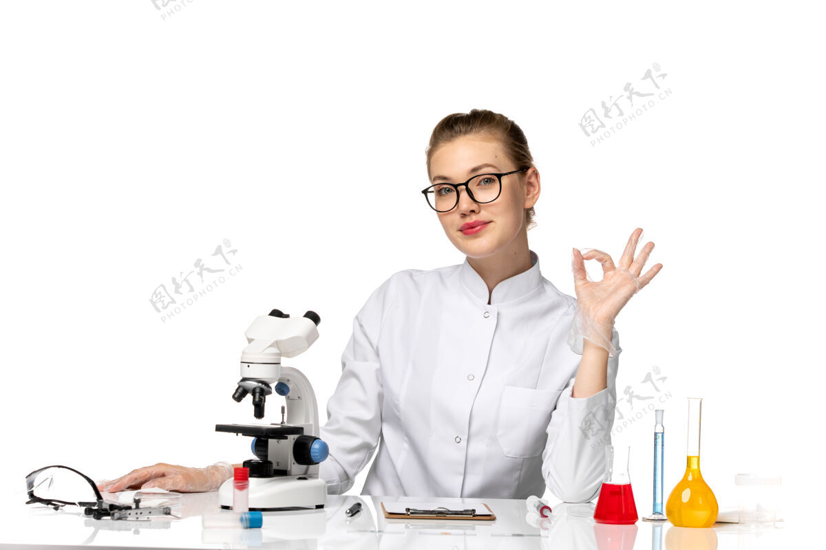 前面前视图穿着白色医疗服的女医生坐在桌子前面 白色空间上有解决方案工作坐病毒