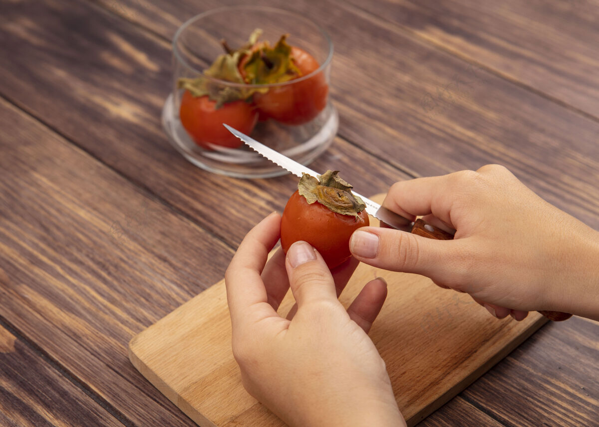 厨房俯视图中的女性手切割一个新鲜的柿子在一个木制的厨房板上用刀在木制表面手食物女