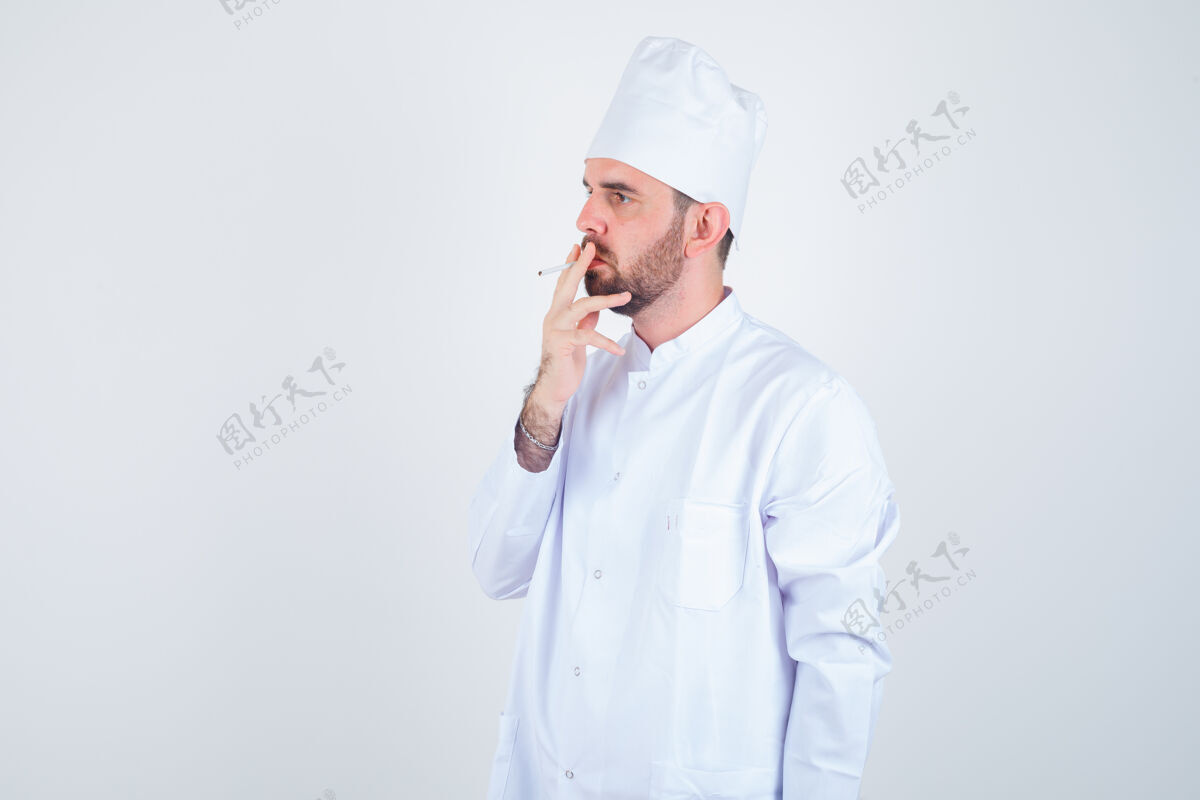 食材年轻男厨师的画像 穿着白色制服抽烟 正看着若有所思的前视图厨师男人思想美味