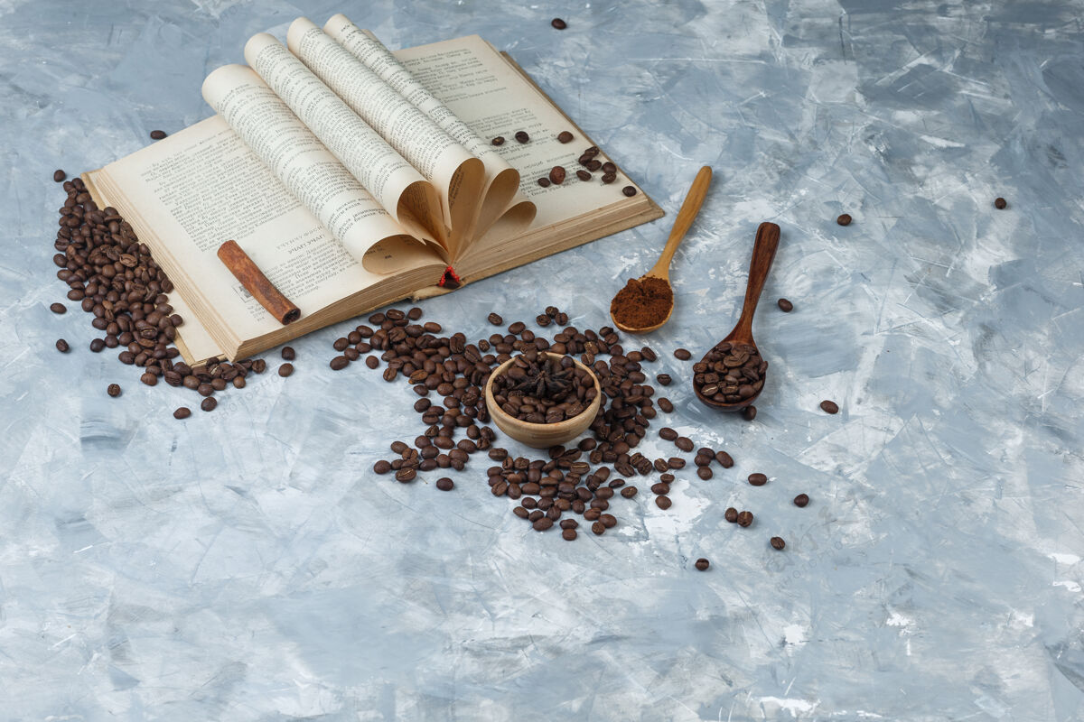 谷物一套磨碎的咖啡 书 肉桂棒和咖啡豆放在碗里 木勺放在一个肮脏的灰色背景上高角度视图高肉桂木头