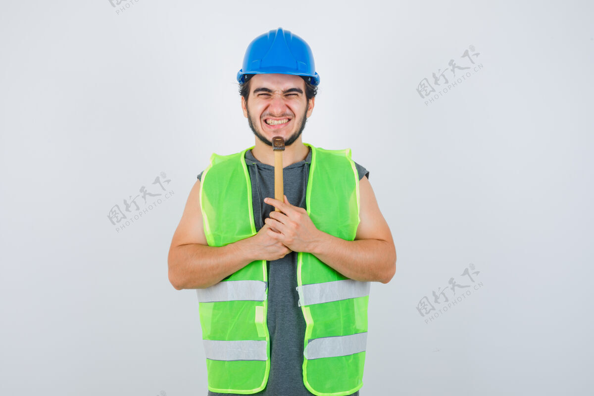 人年轻的建筑工人穿着工装 下巴下拿着锤子 看上去很快乐 正对着窗外肖像胡须男性