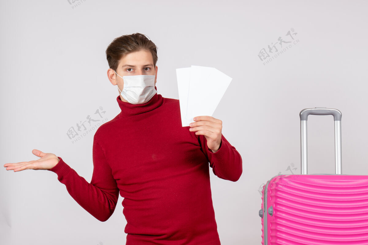 飞机戴着面具的年轻男子在白墙上拿着飞机票的正视图脸前面旅行