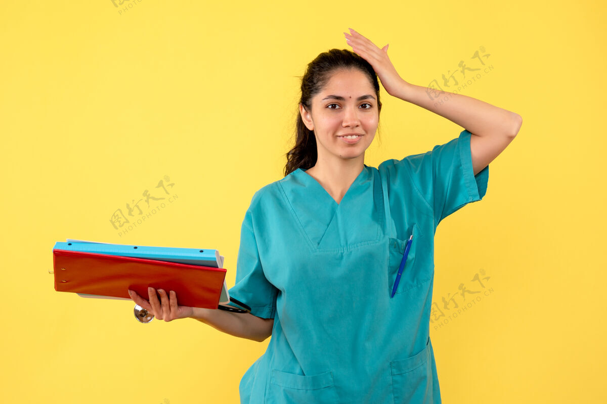 文件夹身着制服的微笑女医生手持文件夹站在黄色的墙上持有人微笑