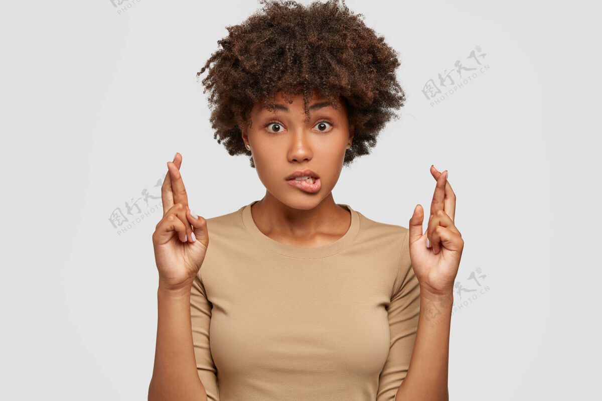 困惑摄影棚拍摄的惊讶的黑人妇女咬下唇 交叉手指爱学生运气