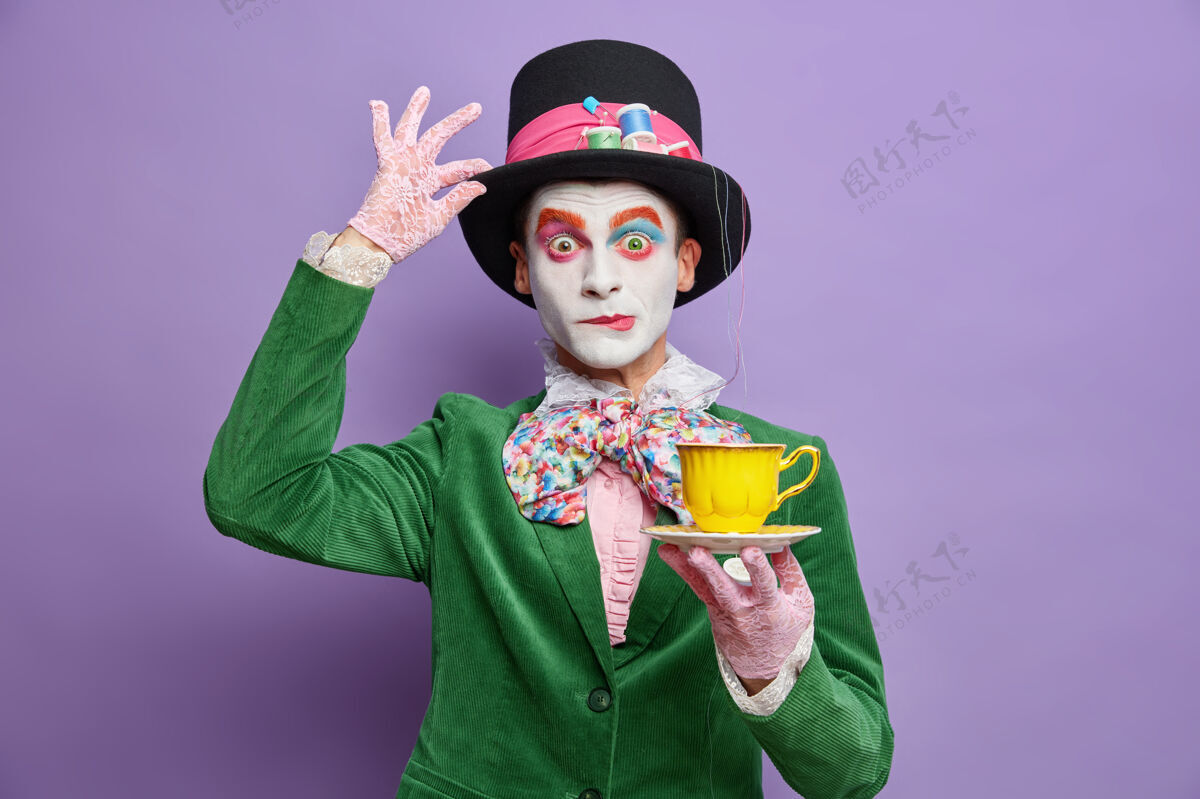 小说喝茶的时间到了化妆亮丽的贵族绅士有虚构人物的形象拿着一杯饮料戴着一顶大帽子在紫色的墙壁上摆出一副奇怪的表情时间幻想仙境