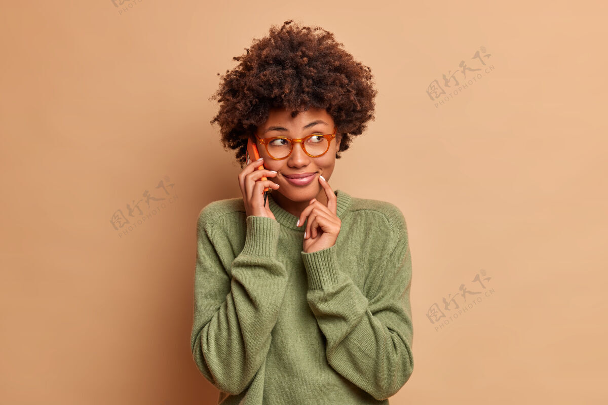 年轻美女笑容可掬的形象和朋友在手机上聊天讨论周末的计划专注在一边愉快地拥有聪明的外表穿着透明眼镜休闲毛衣表情电话手机
