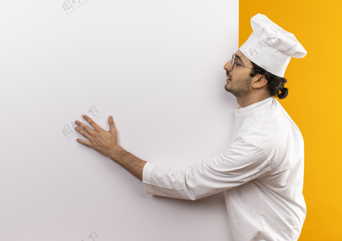 佩戴年轻的男厨师闭着眼睛 穿着厨师制服 戴着眼镜 拿着白色的墙 隔离在黄色的墙上 留着复印空间眼镜制服厨师