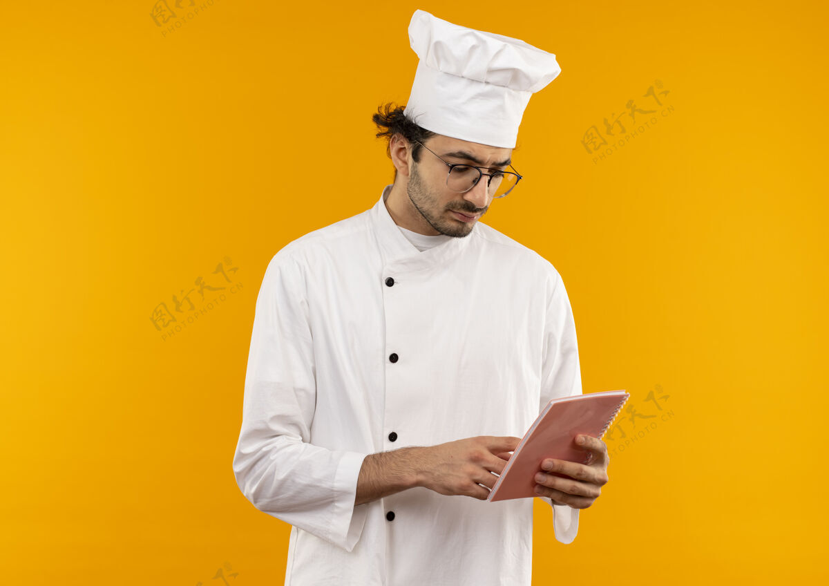 思考想着年轻的男厨师穿着厨师制服戴着眼镜拿着笔记本看着隔离在黄色墙上笔记本年轻男性