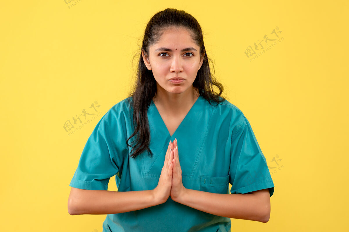 肖像黄色墙上美丽的女医生双手合十的正面图护士成人医生