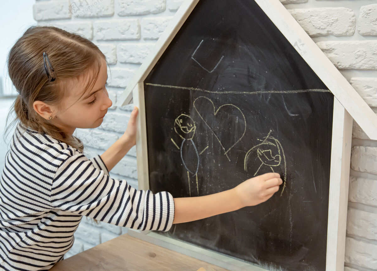 乐趣一个小女孩用粉笔在黑板上画房子的形状房子人孩子