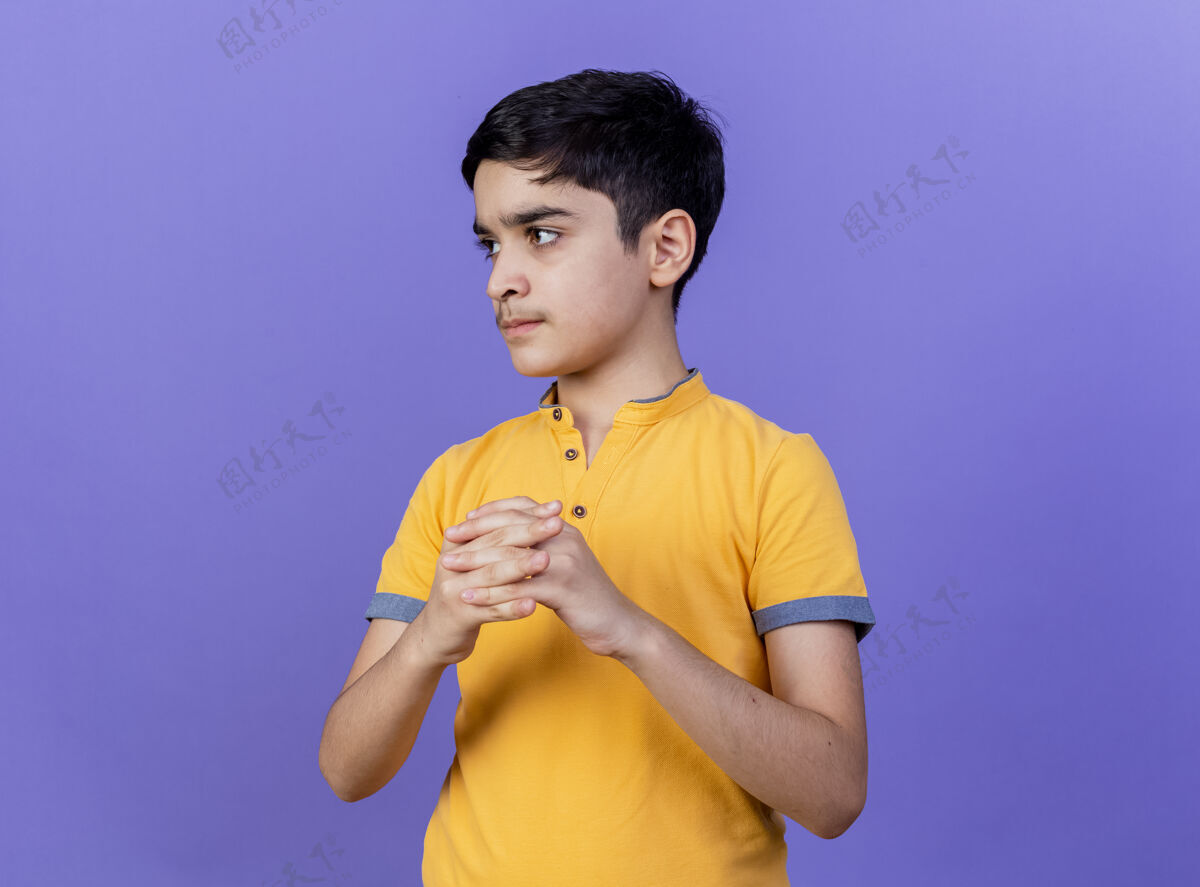 手严格年轻的白人男孩看着一边保持手在一起紫色背景与复制空间隔离保持侧翼男孩