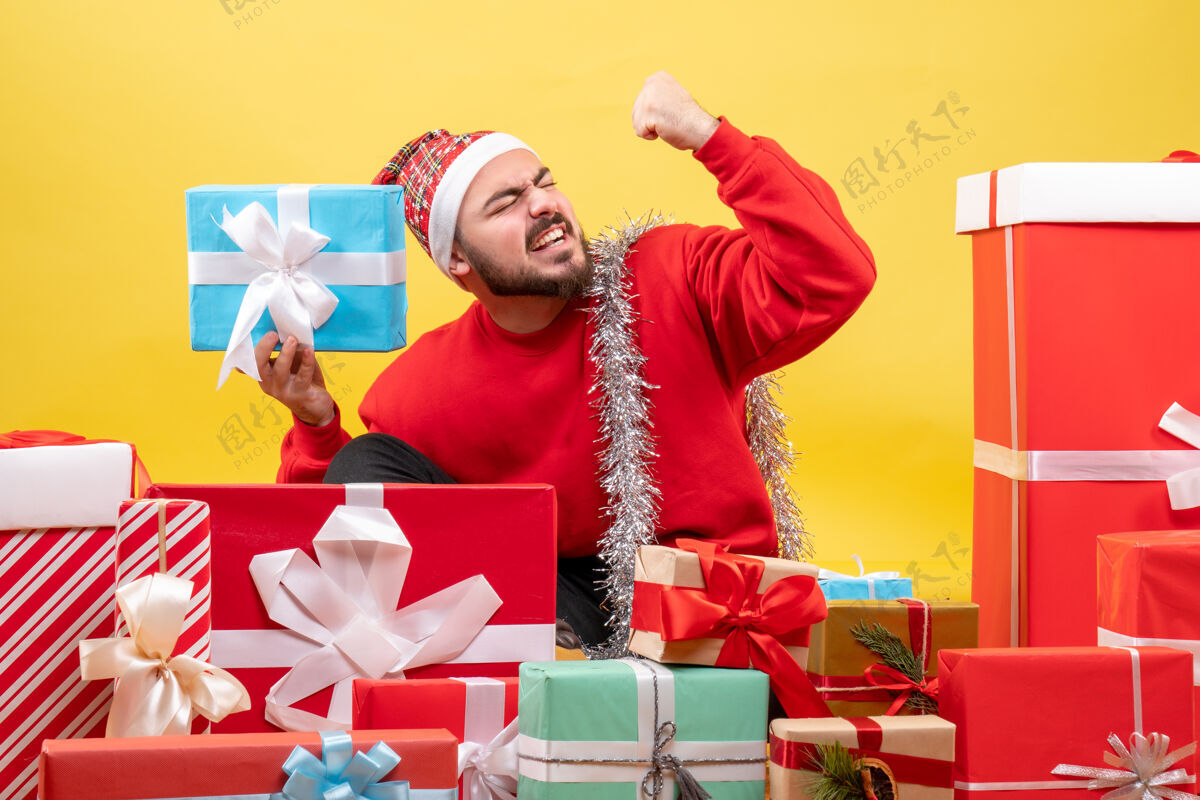 礼物正面图：坐在黄色背景上的年轻男性礼物购物人帽子