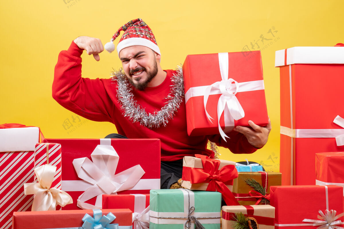 礼物正面图：年轻男性围坐在黄色背景上的圣诞礼物旁生日购物坐着