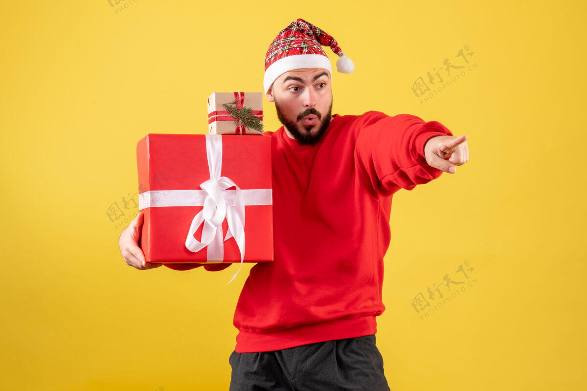 男性黄色背景下手持圣诞礼物的年轻男性正面图圣诞节礼物年份