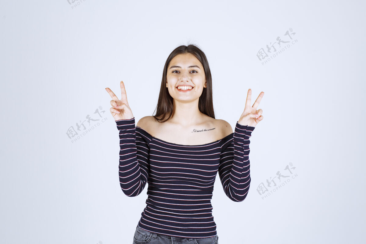 人穿条纹衬衫的年轻女子发出和平信号成人人类微笑
