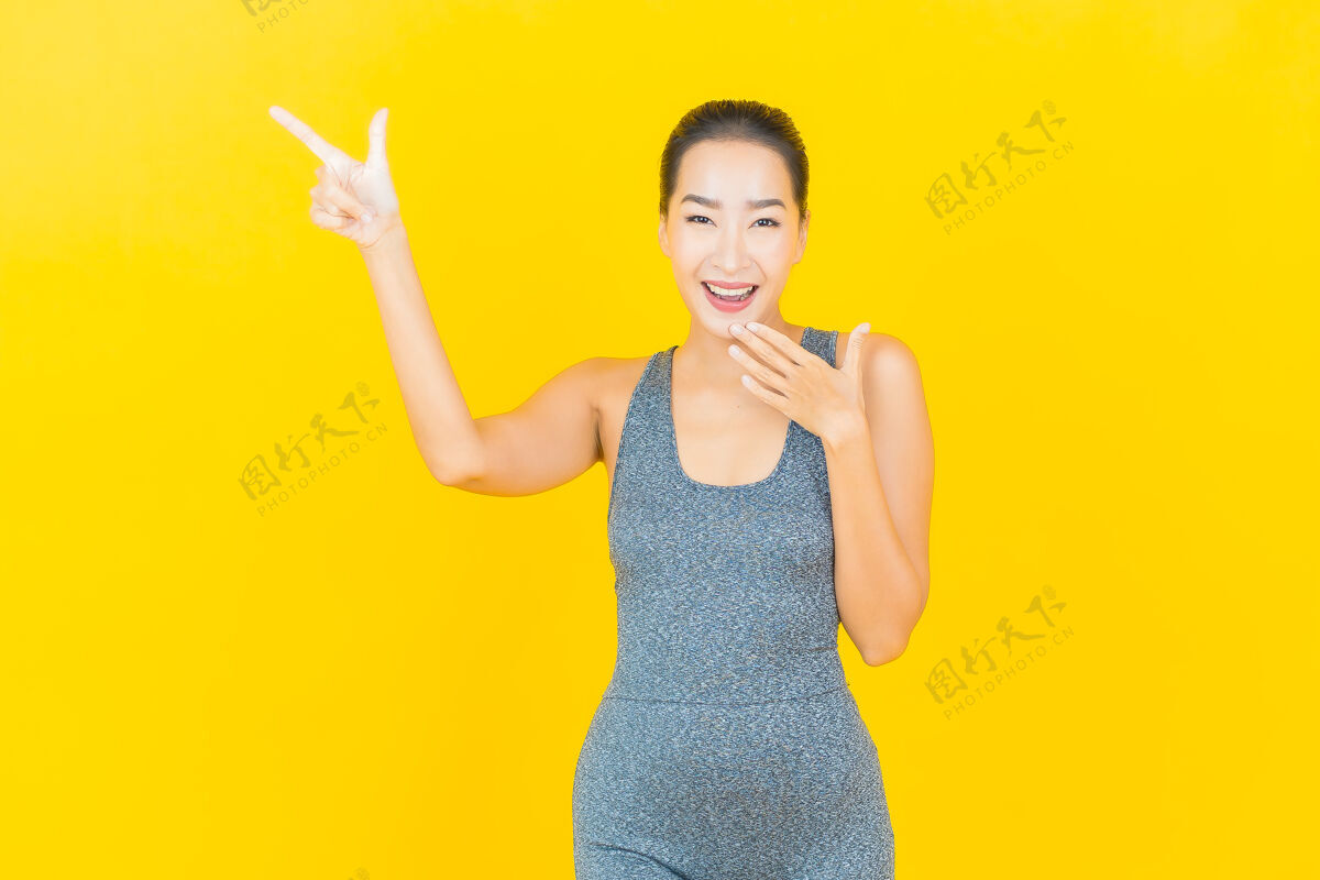 发光在黄色的墙上 描绘一位穿着运动服准备锻炼的美丽亚洲年轻女子女孩性感微笑