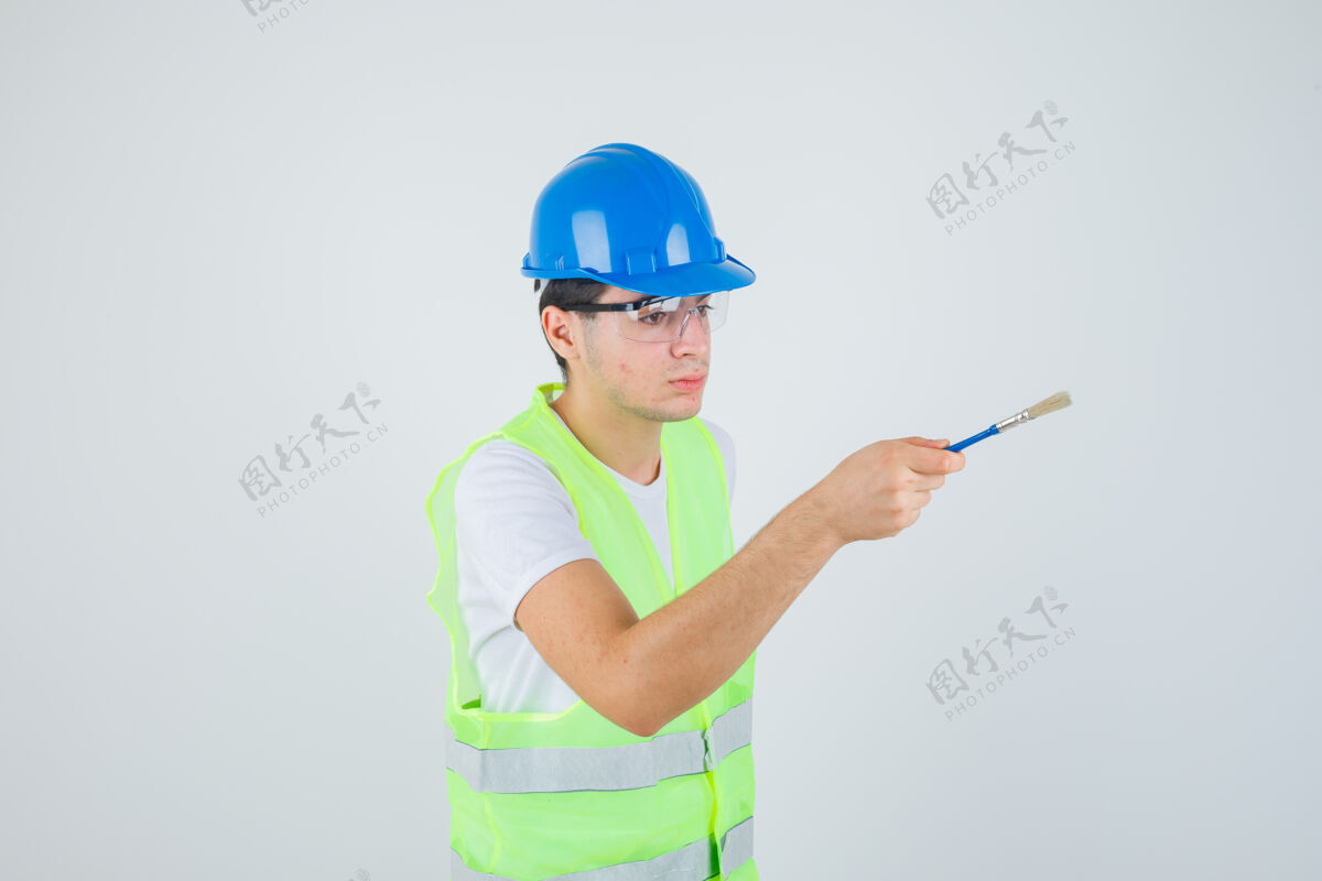 建筑小男孩拿着油漆刷 试图把它交给一个穿着建筑制服的人 看起来很专注前视图油漆幼儿制服