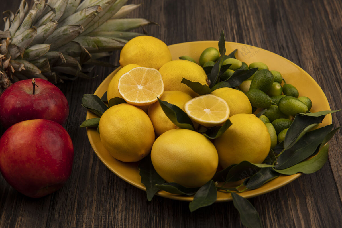 顶部顶视图富含维生素的水果 如柠檬和金盏花在黄色的盘子上 菠萝和红苹果被隔离在木制的墙上膳食饮食素食