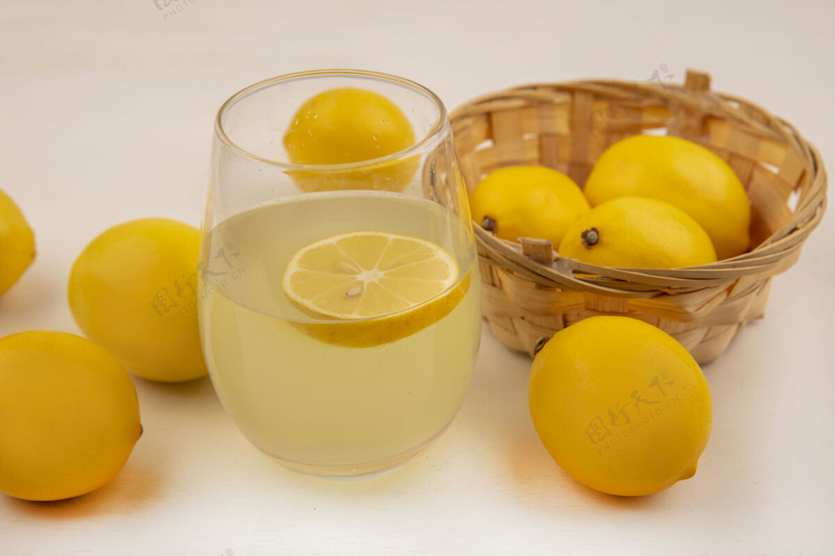 柑橘白色墙壁上一个装着新鲜柠檬汁的水桶上的新鲜柠檬俯视图食品柠檬桶